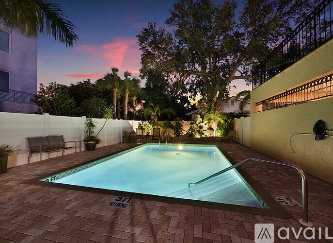 A pool surrounded by a brick patio and a white fence.