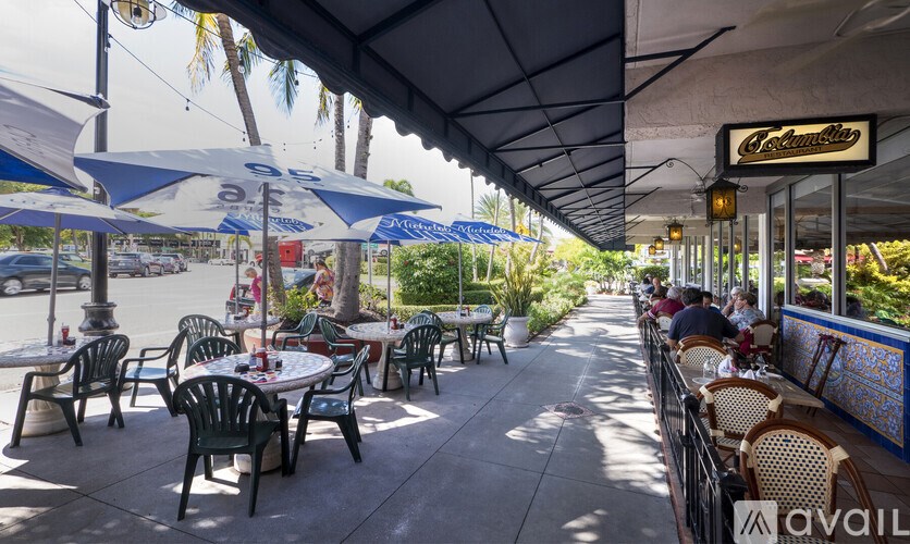A restaurant with tables and chairs under umbrellas and a blue awning.