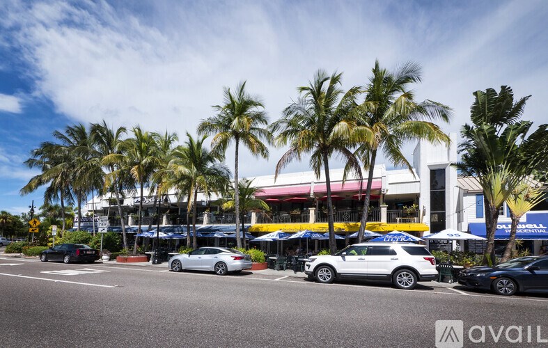 A sunny day at the beach with palm trees and cars parked by the storefronts.