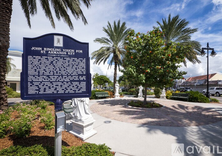 A blue sign with white text stands in front of a statue and trees.