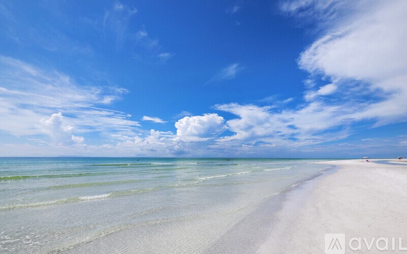 A beach with white sand and clear blue water under a blue sky with clouds.