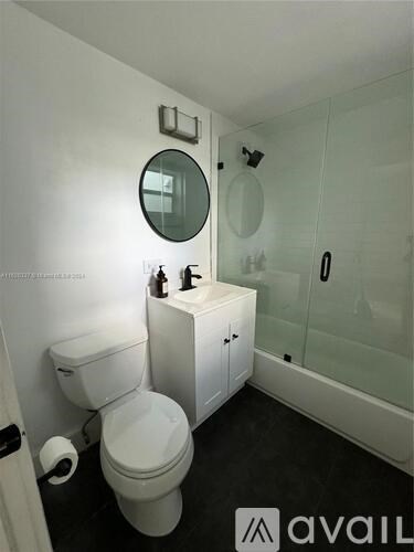 A white toilet with a toilet paper roll on the side and a round mirror above it.