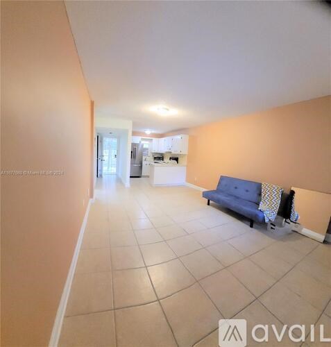 A living room with a blue sofa and a kitchen in the background.