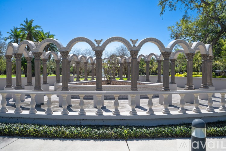 A white arched fence with a row of bushes in front.