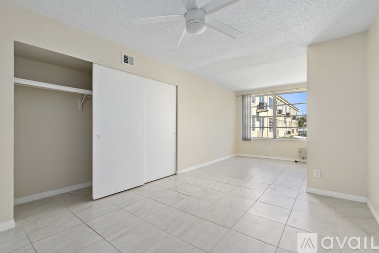 A room with a white ceiling fan and a large window with a view of buildings outside.