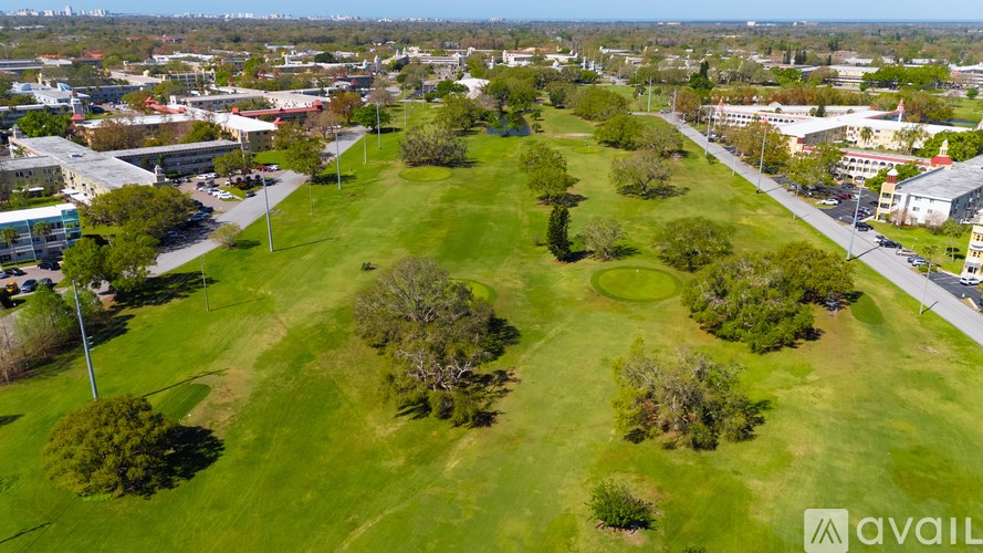 A grassy field with trees and buildings in the distance.