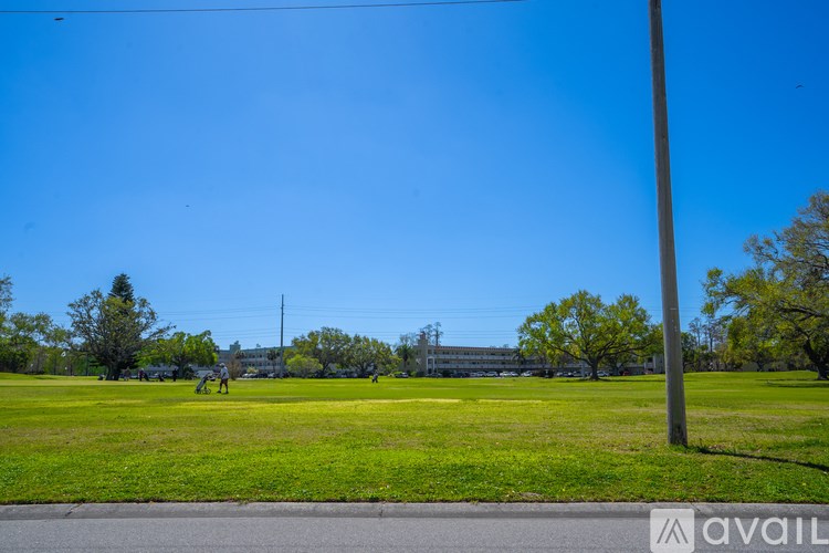 A grassy field with a clear blue sky and a few trees in the distance.
