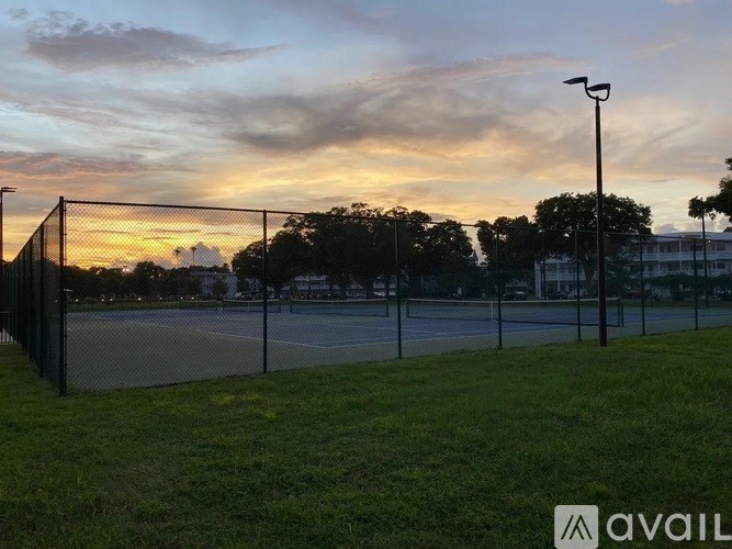 Tennis court surrounded by a fence with trees in the background.