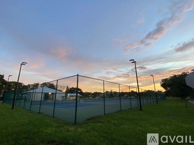 Tennis court surrounded by a fence with a cloudy sky in the background.