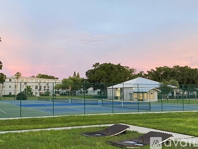 A tennis court surrounded by a fence with a building in the background.