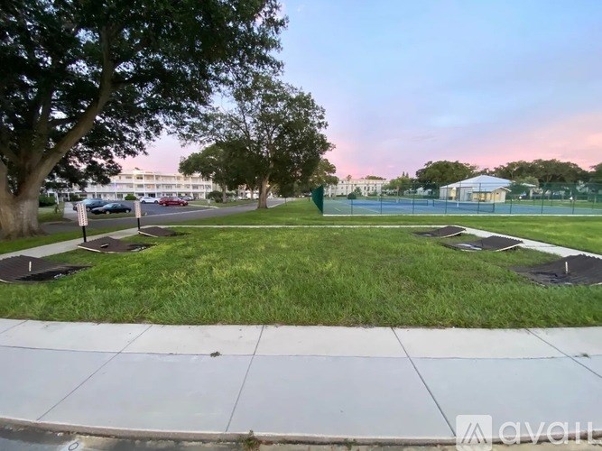 A park with a tennis court and a building in the background.