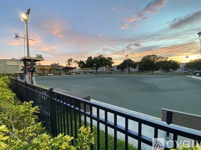 A view of a pool area with a fence and a building in the background during sunset.