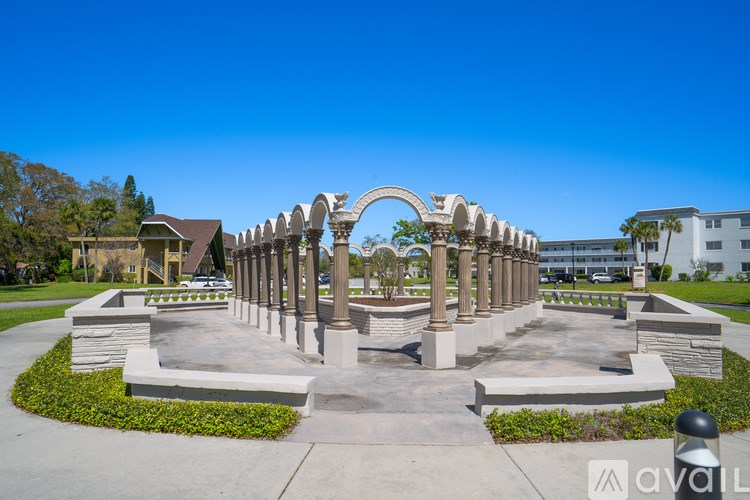 A park with a large arched structure and a pavilion in the background.