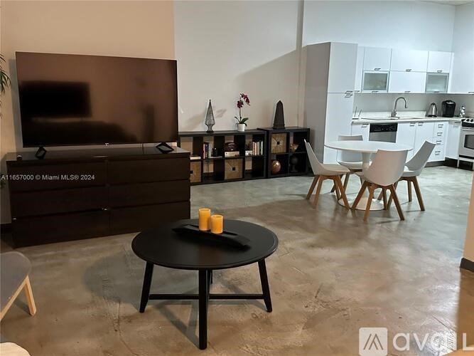 A living room with a black table and chairs, a television, and a dining area in the background.