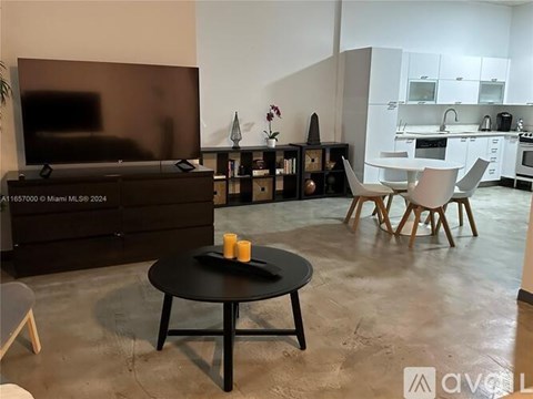 A living room with a black table and chairs, a television, and a dining area in the background.