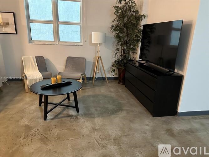 A living room with a black sofa, a grey armchair, a round table, and a television.