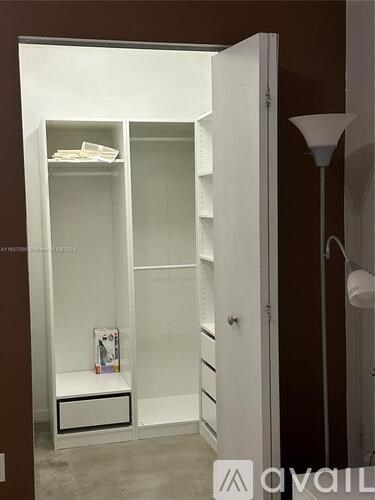 A white wardrobe with shelves and drawers is open, revealing a lamp and a picture frame on the floor.