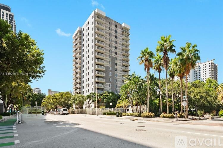 A tall residential building is surrounded by palm trees and other greenery.