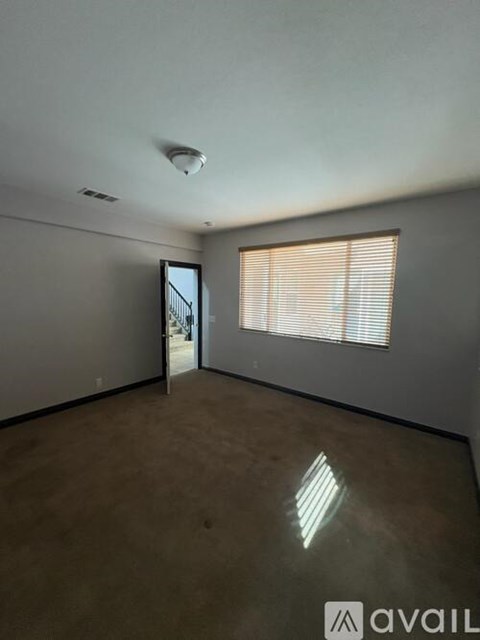 A room with a window covered by blinds and a door leading to another room.