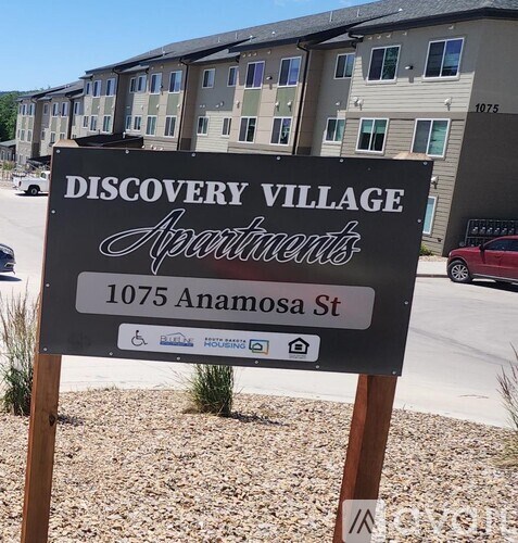 A sign for Discovery Village Apartments stands in front of apartment buildings.