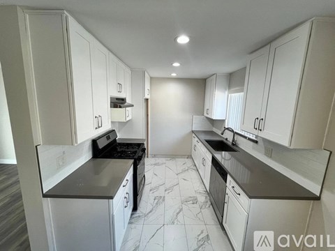 A kitchen with white cabinets and marble flooring.