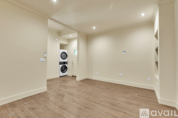 A spacious room with wooden flooring and a washing machine in the corner.