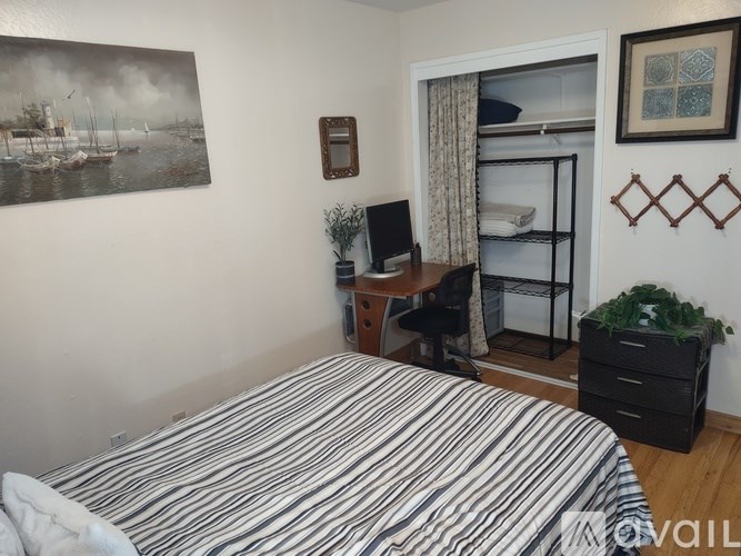 A bedroom with a bed, desk, chair, and a painting on the wall.
