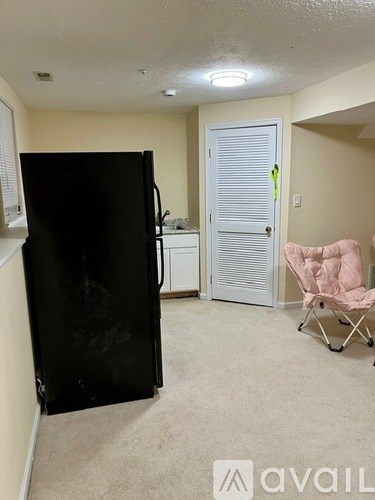 A black refrigerator is in a kitchen with a pink chair.