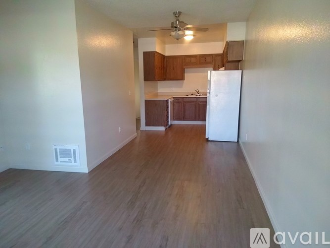 A kitchen area with a refrigerator, wooden floors, and a ceiling fan.