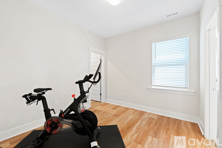 A black exercise bike is on a black mat in a white room.