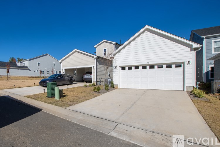 A white house with a garage is in front of a blue car.
