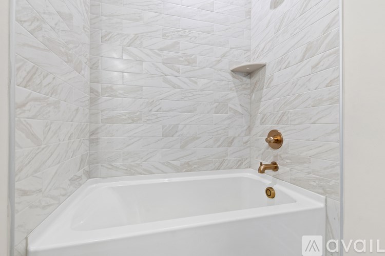 A white bathtub with gold fixtures in a bathroom with white marble tile walls.