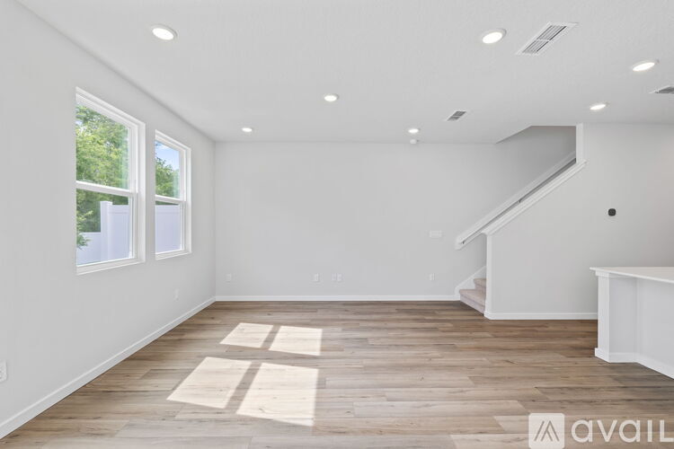 A spacious room with wooden flooring and a staircase on the right side.