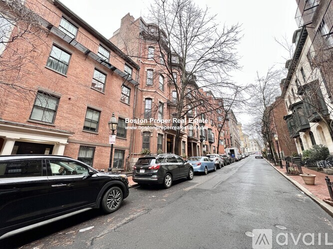 A street view of a residential area with parked cars and brick buildings.
