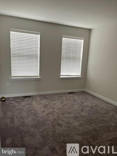 A room with carpeted floor and two windows with blinds.
