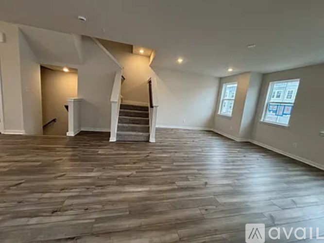 A spacious room with wooden flooring and a staircase in the background.