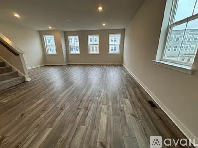 A spacious room with wooden flooring and a staircase on the left side.