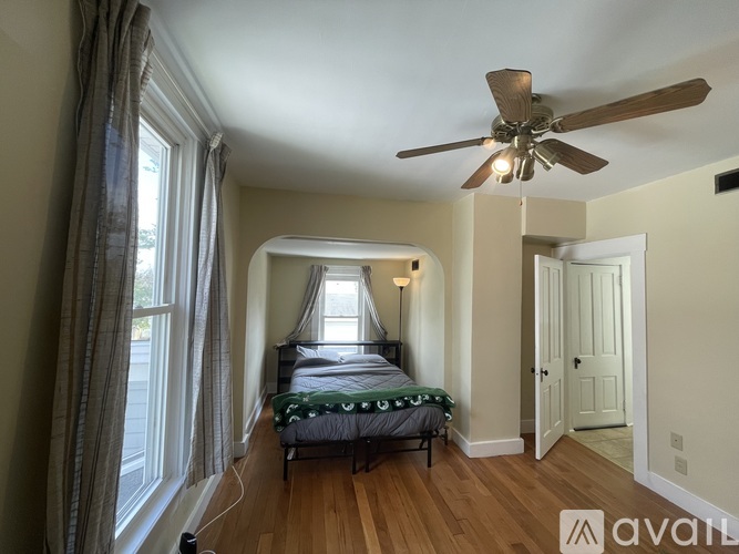 A bedroom with a bed, a window with curtains, and a ceiling fan.