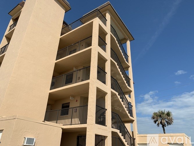 A tall beige apartment building with balconies and a palm tree in the background.