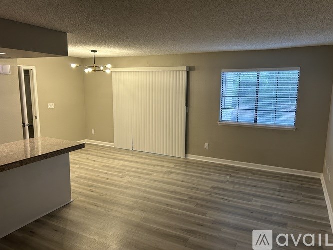 A spacious room with wooden flooring and a window with blinds.