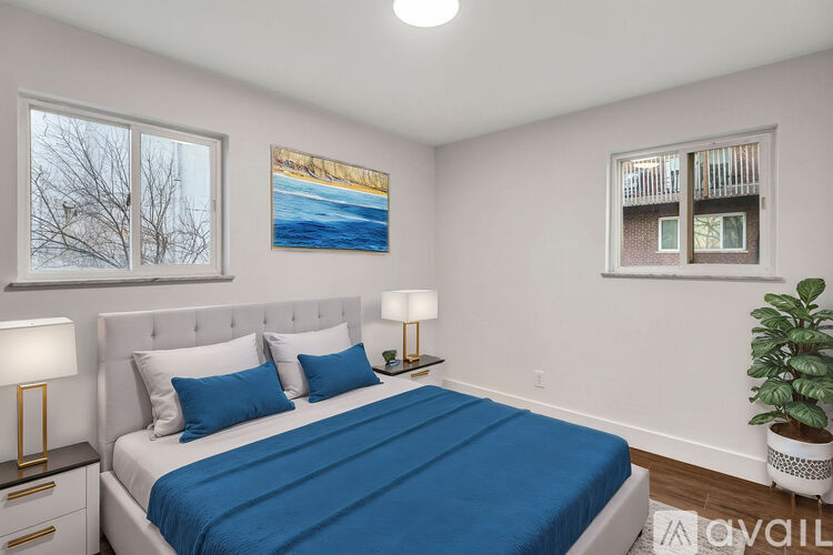 A bedroom with a bed, two lamps, a potted plant, and pictures on the wall.