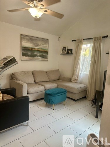 A living room with a beige couch, a blue ottoman, and a painting on the wall.