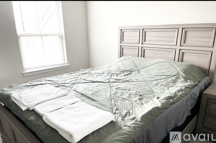 A bed with a green comforter and white towels is in a room with a window.