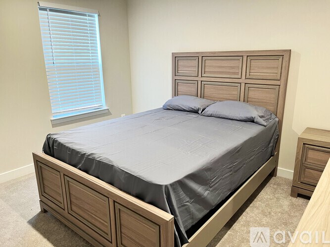 A bed with a grey cover and two pillows is in a room with a window.