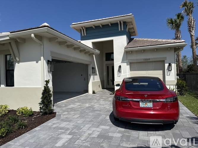 A red car is parked in front of a two-story house.