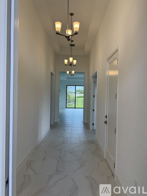 A long hallway with a chandelier and doors on both sides.
