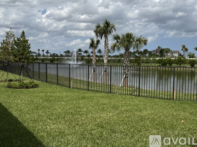 A grassy area with a fence and trees in front of a body of water.