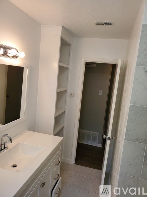 A bathroom with a sink, mirror, and a doorway leading to another room.