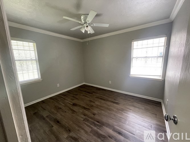 A room with a ceiling fan and two windows.