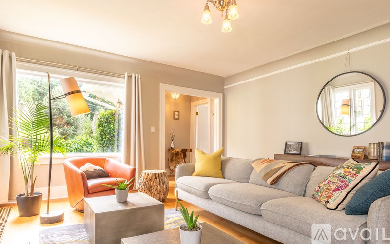 A living room with a grey couch, a round mirror, and a chandelier.